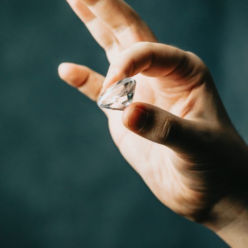 A hand grabbing a diamond with copy space over a dark background