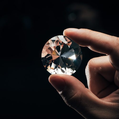 cropped view of man holding big clear shiny diamond on black background